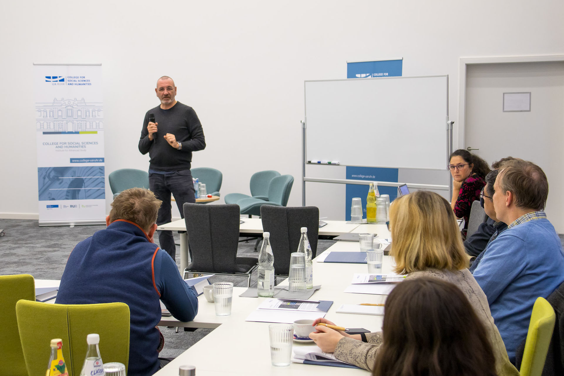 photo from the workshop, Prof. Gudehus standing and presenting, six participants sitting at tables