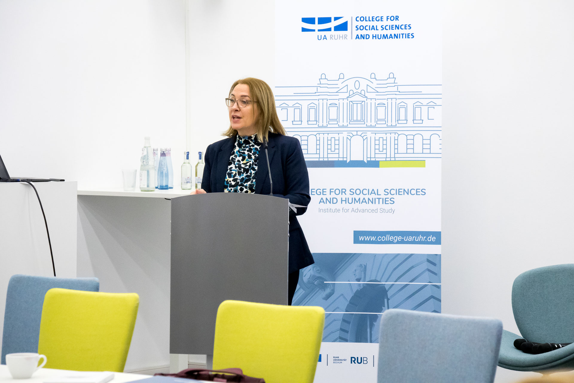 photo from the workshop 'Perpetrator Memory in Spanish culture', participants sitting around a table, a speaker presenting, a screen with slides in the back