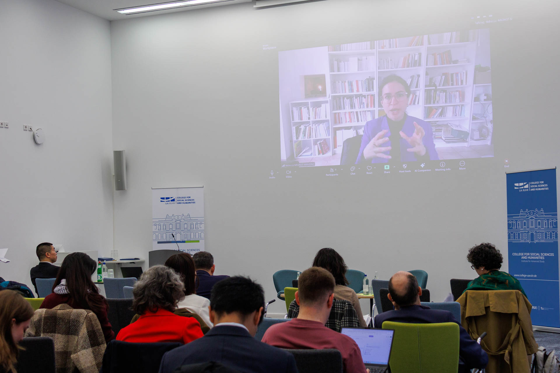 photo from the conference, speaker addressing the audience via digital screen